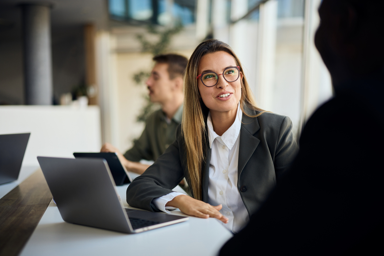 A business professional with a laptop talking to a colleague. 