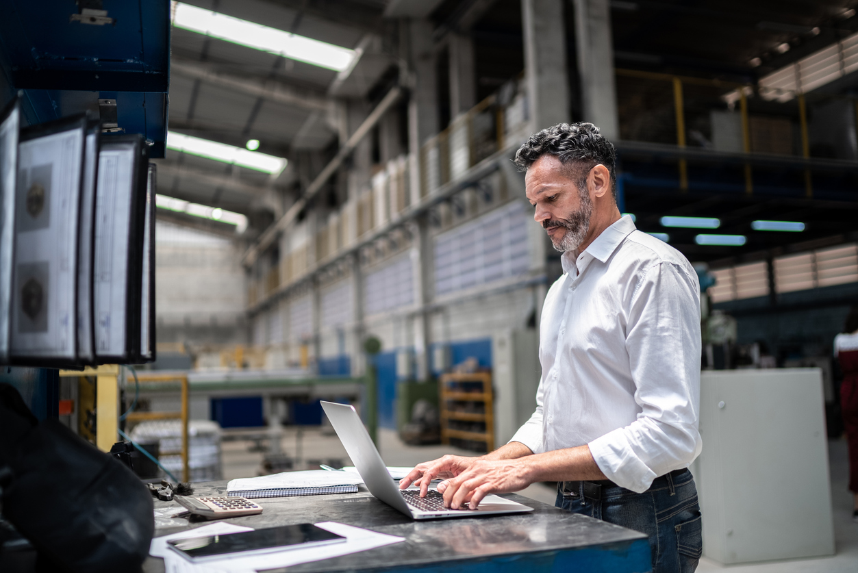 Supply chain manager working in a manufacturing facility on a laptop.